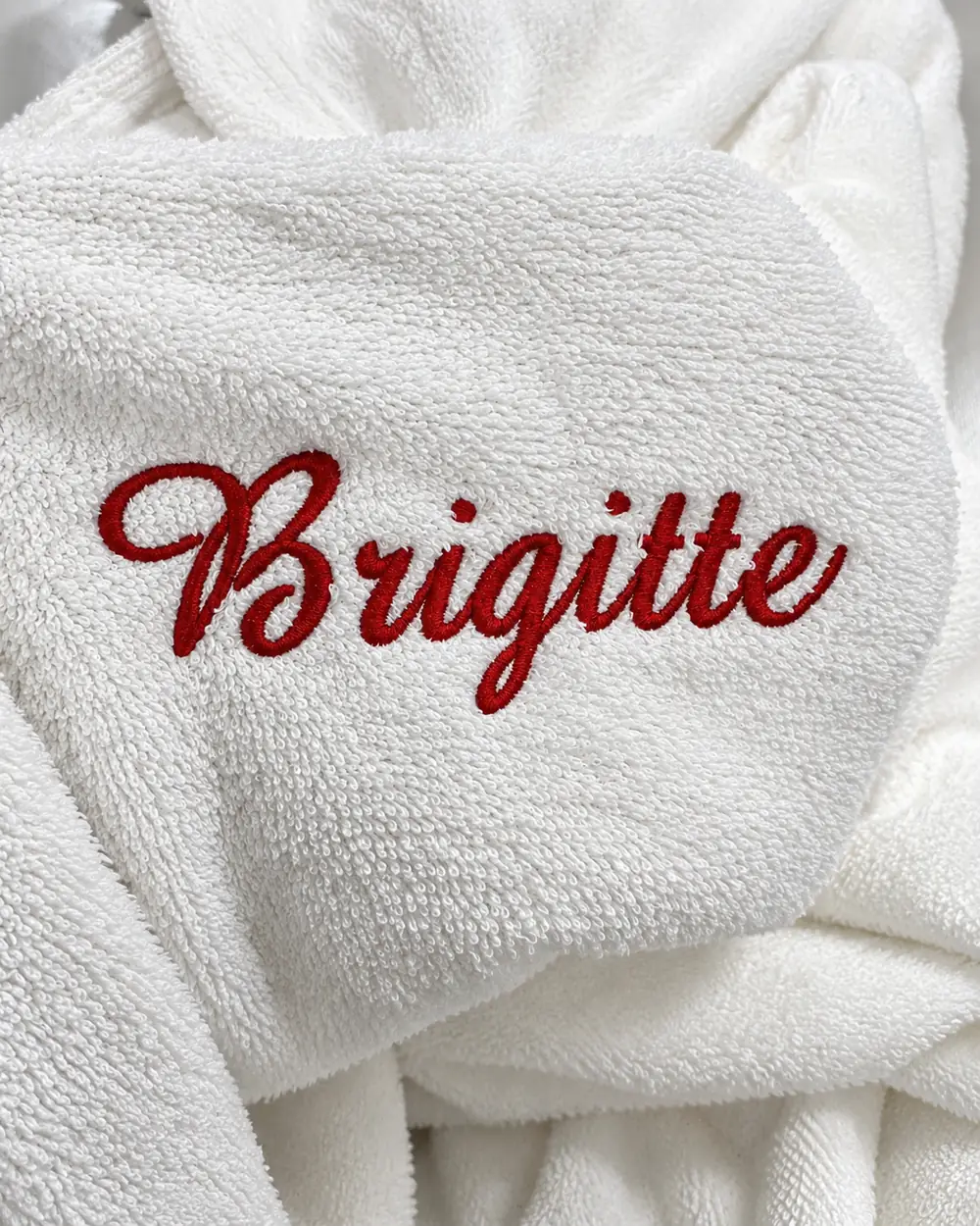 Peignoir blanc brodé au prénom « Brigitte » en fil rouge, pour la mariée