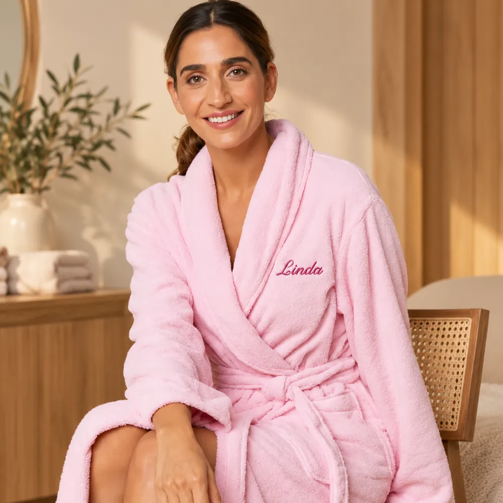 Femme portant un peignoir personnalisé rose, brodé au prénom « Linda » en fil fuchsia